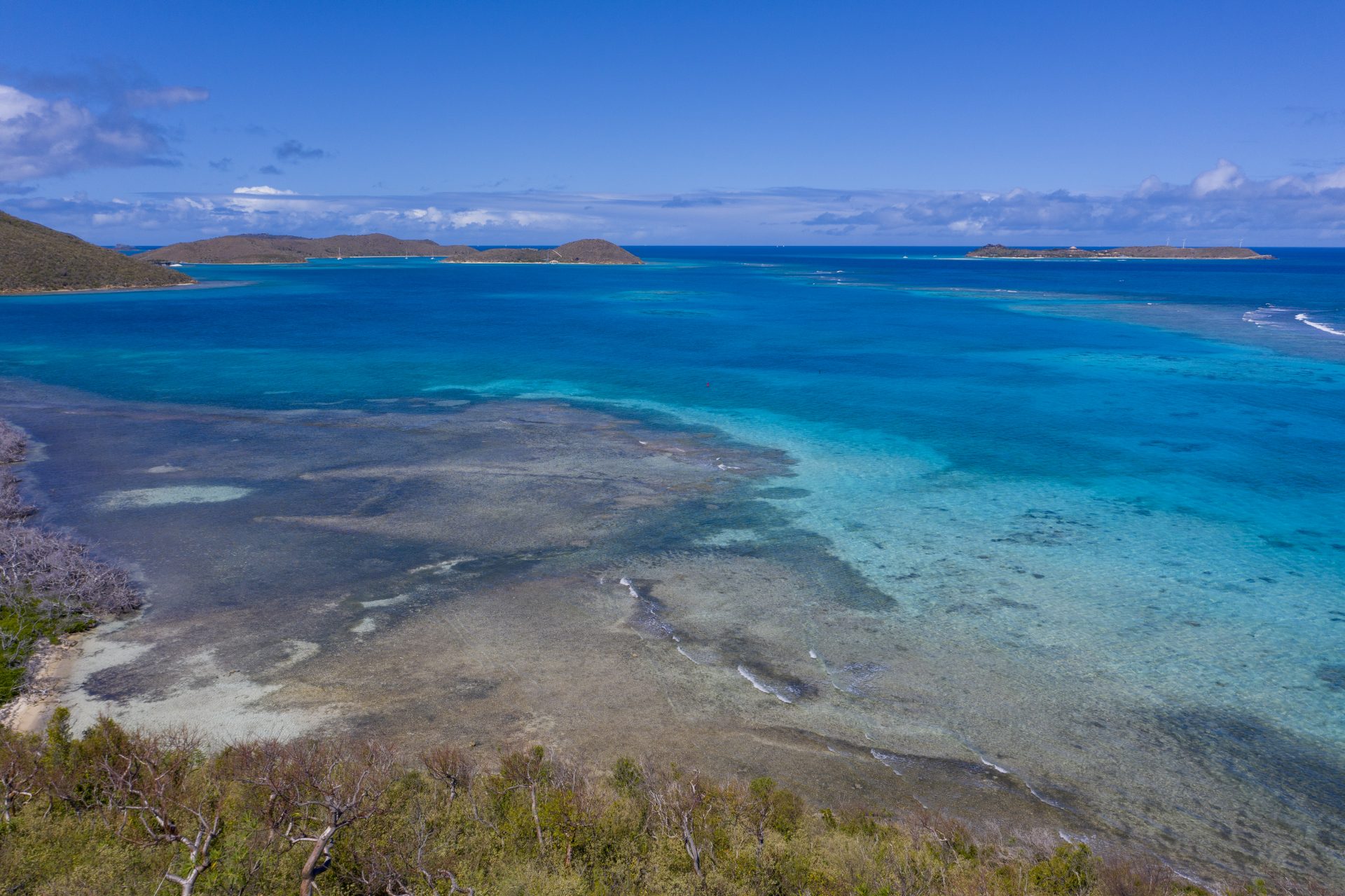 A tranquil seascape showcasing clear turquoise waters gently lapping against a sandy beach in the foreground, with lush green islands and rocky outcrops dotting the background under a bright blue sky, creating an idyllic setting for your dream estate.