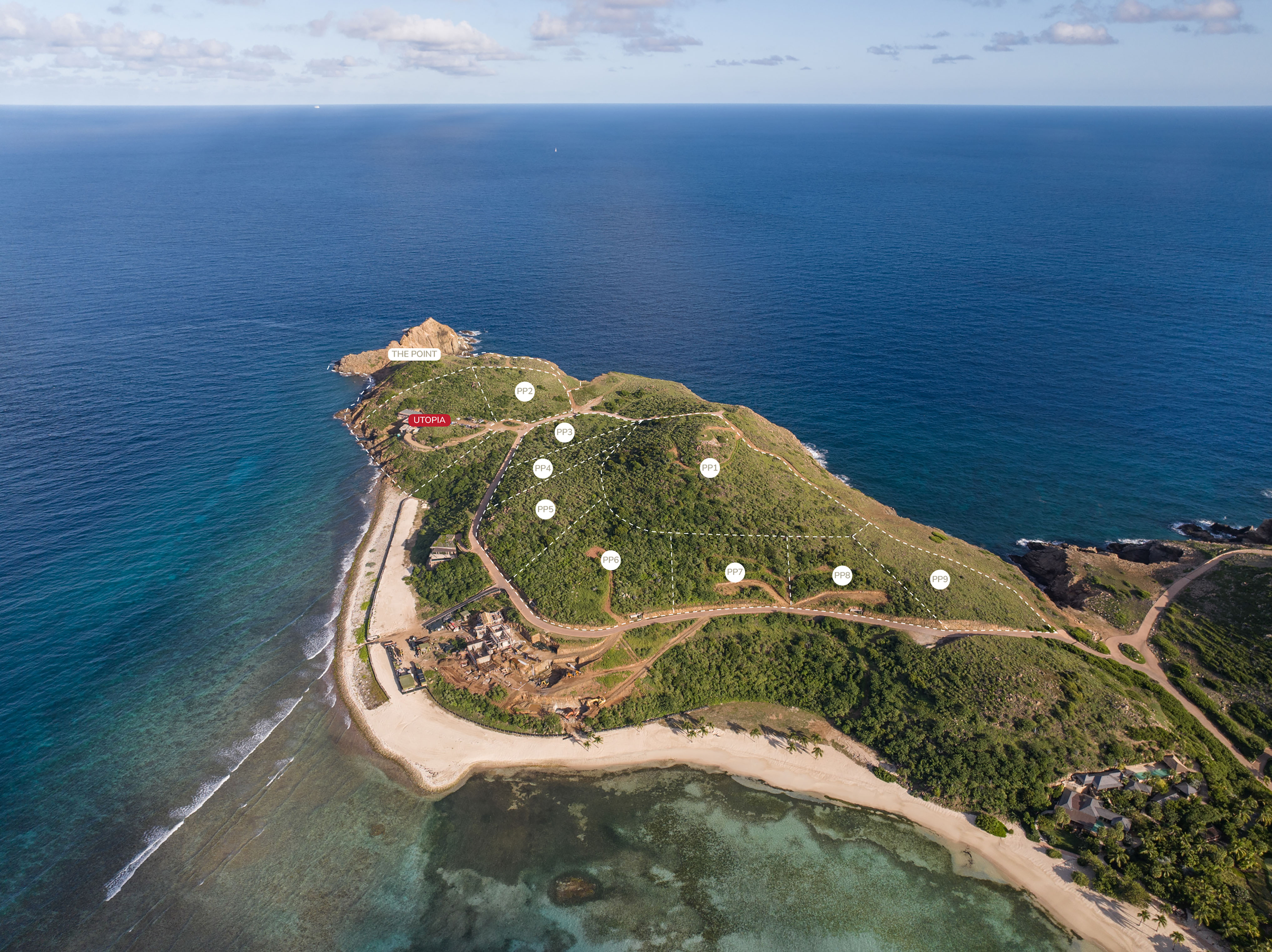 Aerial view of a small green island, Pajaros Point, surrounded by clear blue ocean. A sandy beach is visible, alongside winding pathways and several quaint structures. A larger building sits prominently at the island's tip, near the water.