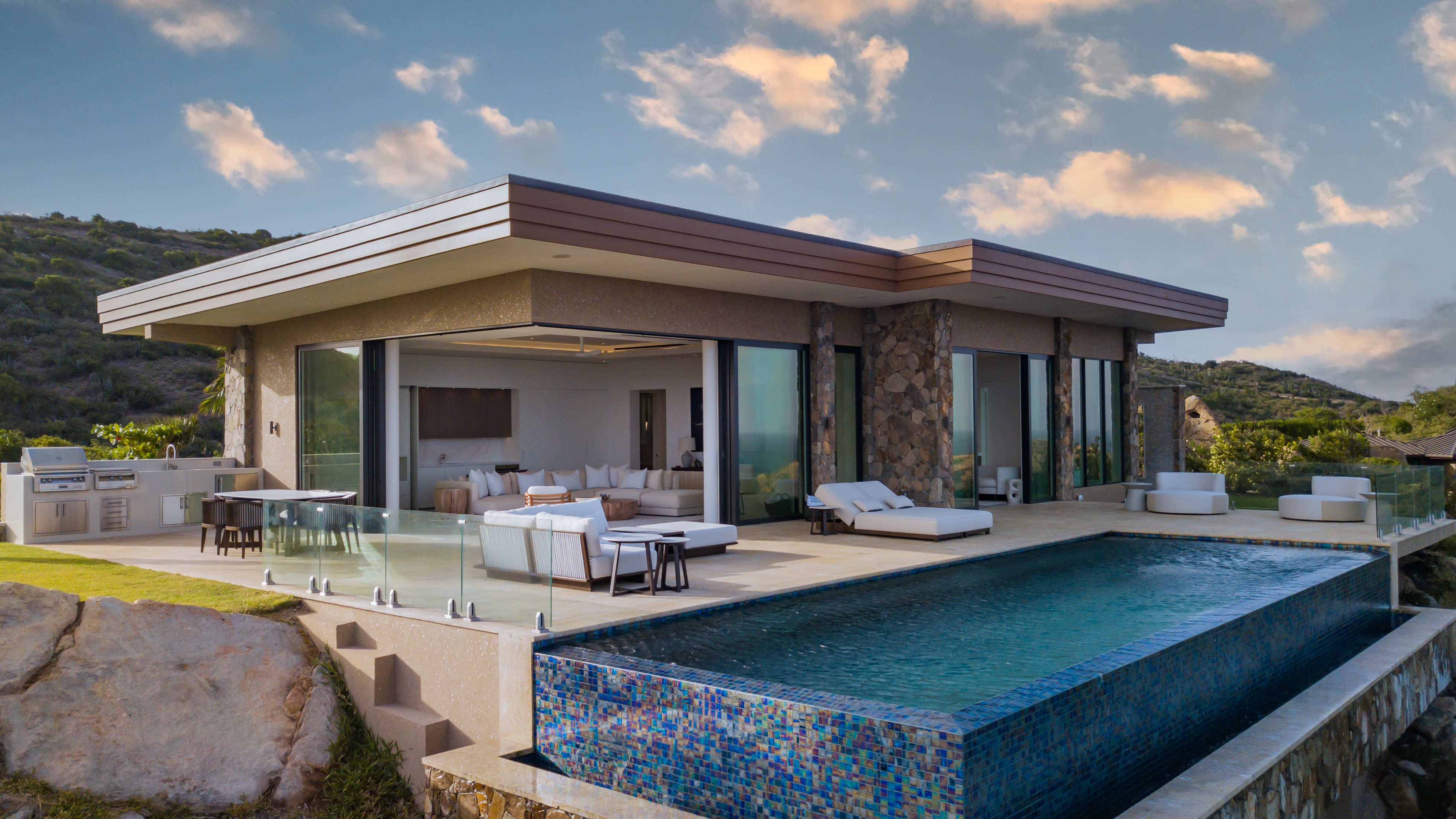 Starlight Villa is a modern luxury villa with floor-to-ceiling glass doors, an infinity pool, outdoor seating, and scenic views of hills and sky. The minimalist design emphasizes clean lines and open spaces, blending seamlessly with the natural surroundings.