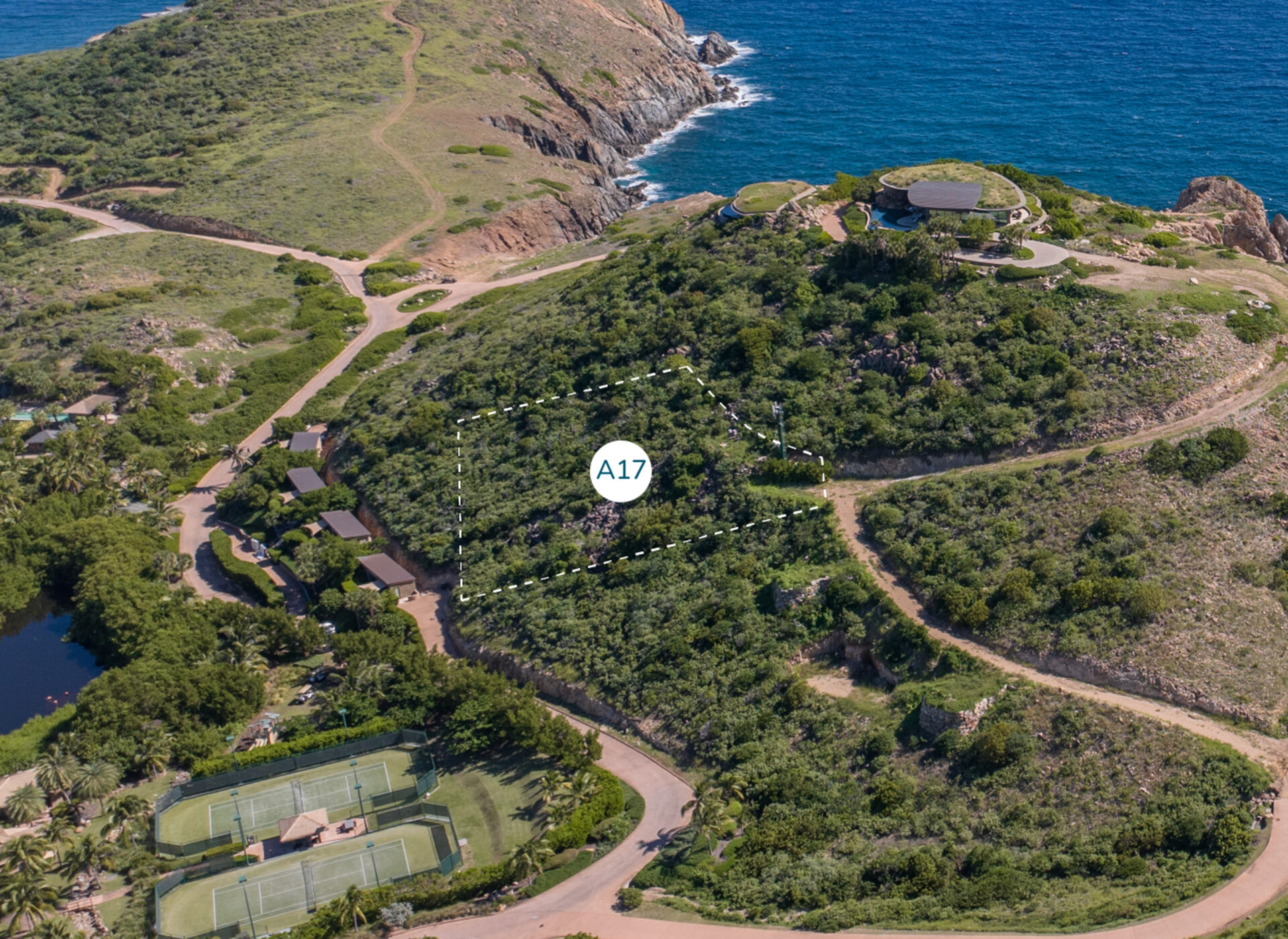 A scenic aerial view of a coastal hilly area with lush greenery. Walking paths wind through the landscape, leading to a marked plot of land labeled "Homesite A17" near the center. Tennis courts and a pond are visible in the bottom left, with Atlantic Ridge in the background.