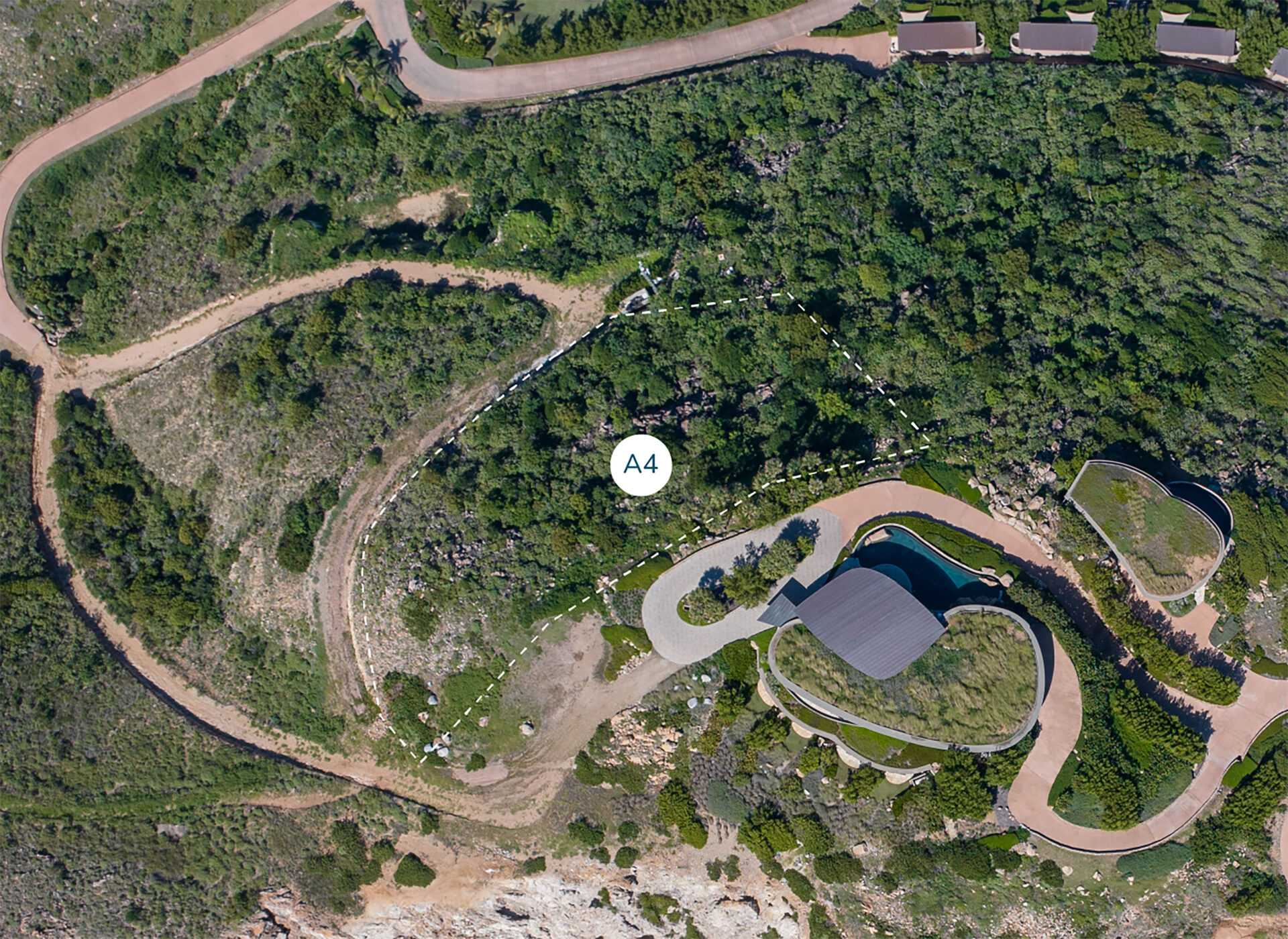 Aerial view of a winding road in a hilly, green landscape leading to a modern building with a curved design and a swimming pool. Various pathways and dense vegetation surround Atlantic Ridge Homesite A4, marked with a circular label "A4" at the center.