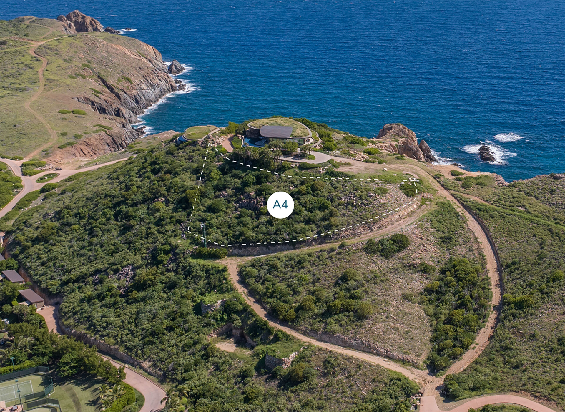 Aerial view of a lush green hill with winding paths leading to Homesite A4 at the summit, marked clearly. The house offers breathtaking views of Atlantic Ridge's rocky coastline and the ocean extending to the horizon. Additional winding trails weave along the slopes of the hill.