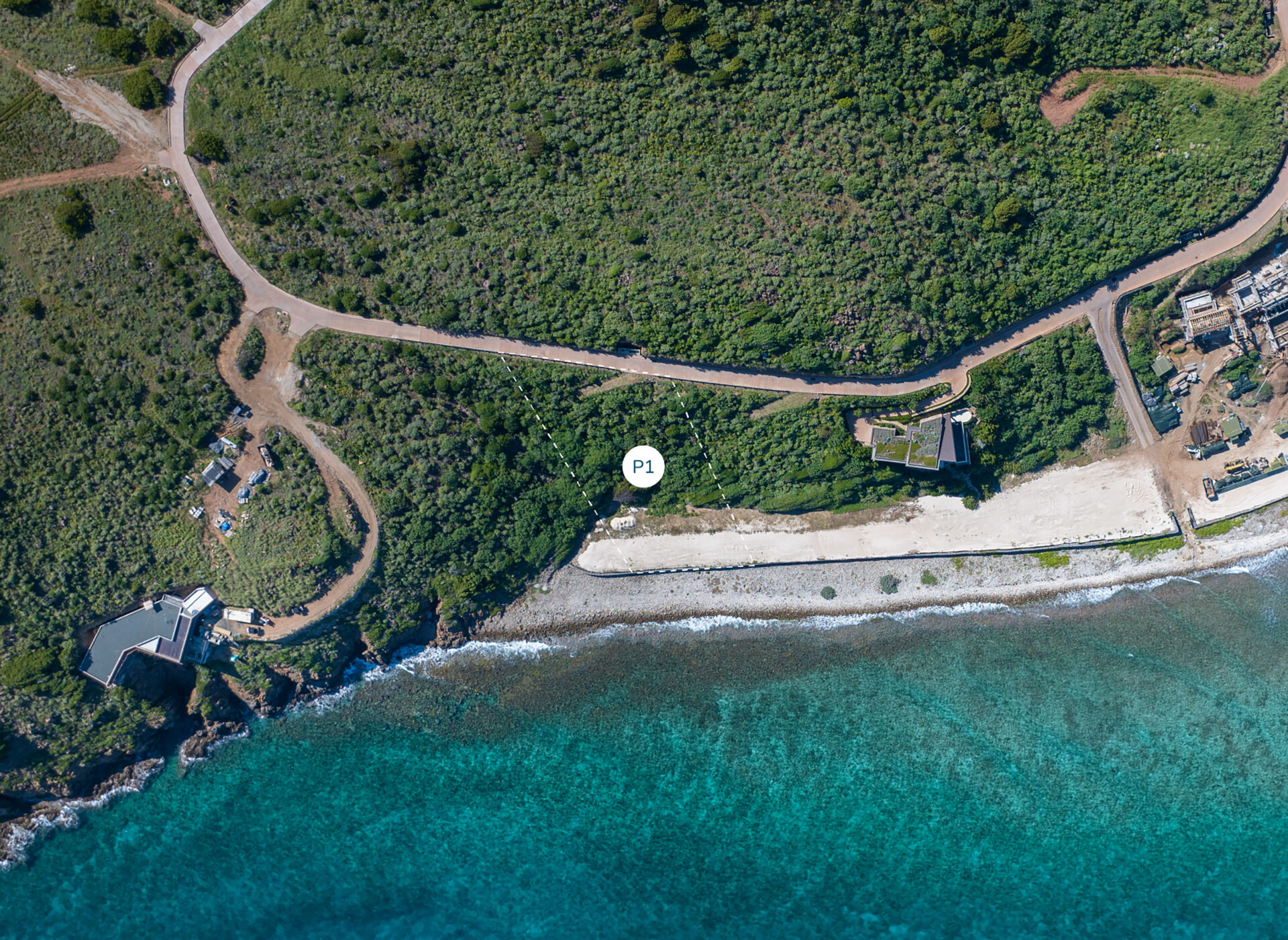 Aerial view of a coastal area with a turquoise ocean, sandy beach, and green foliage. A road winds through the vegetation towards Peninsula Homesite while structures are scattered near the shore. A marked point labeled "P1" is visible near the beach, with another point "P2" indicating an adjacent location.