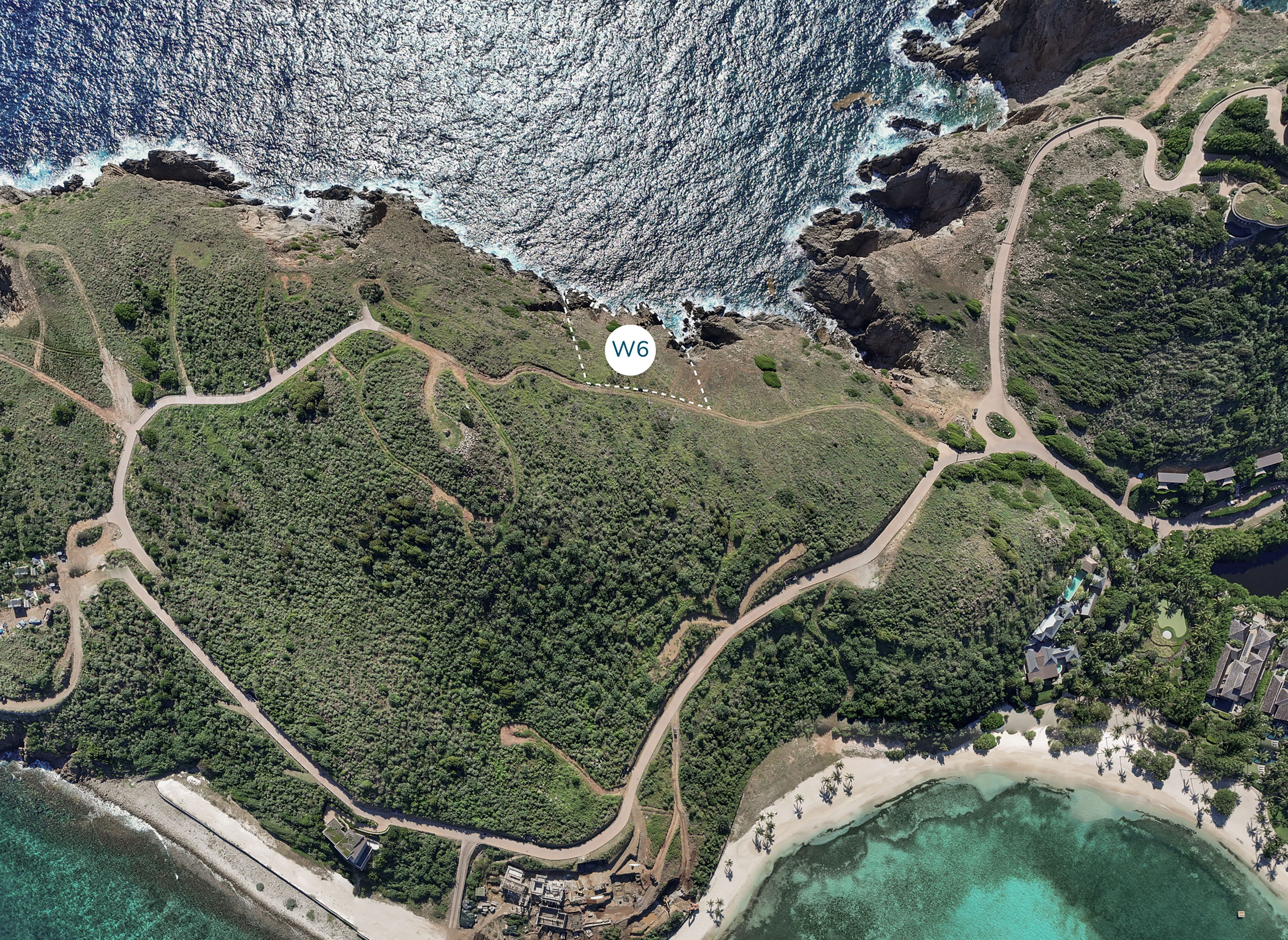 An aerial view of a coastal area with a rugged terrain featuring numerous winding paths. The ocean is on the left with waves crashing against the rocky shore. On the right, there is a sandy beach near some buildings. A white circle labeled "Wildside Homesite W6" is marked in the center.