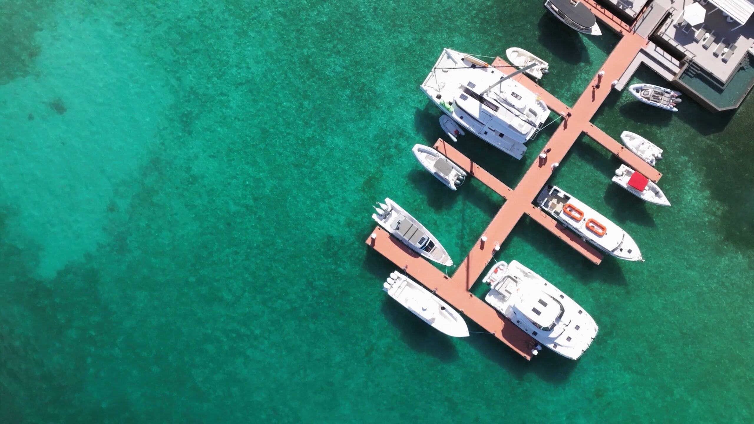 Aerial view of Marina Village shows boats docked along wooden piers extending into clear turquoise water. The boats vary in sizes, and the surrounding water is calm, showcasing the vibrant color and clarity of the ocean.