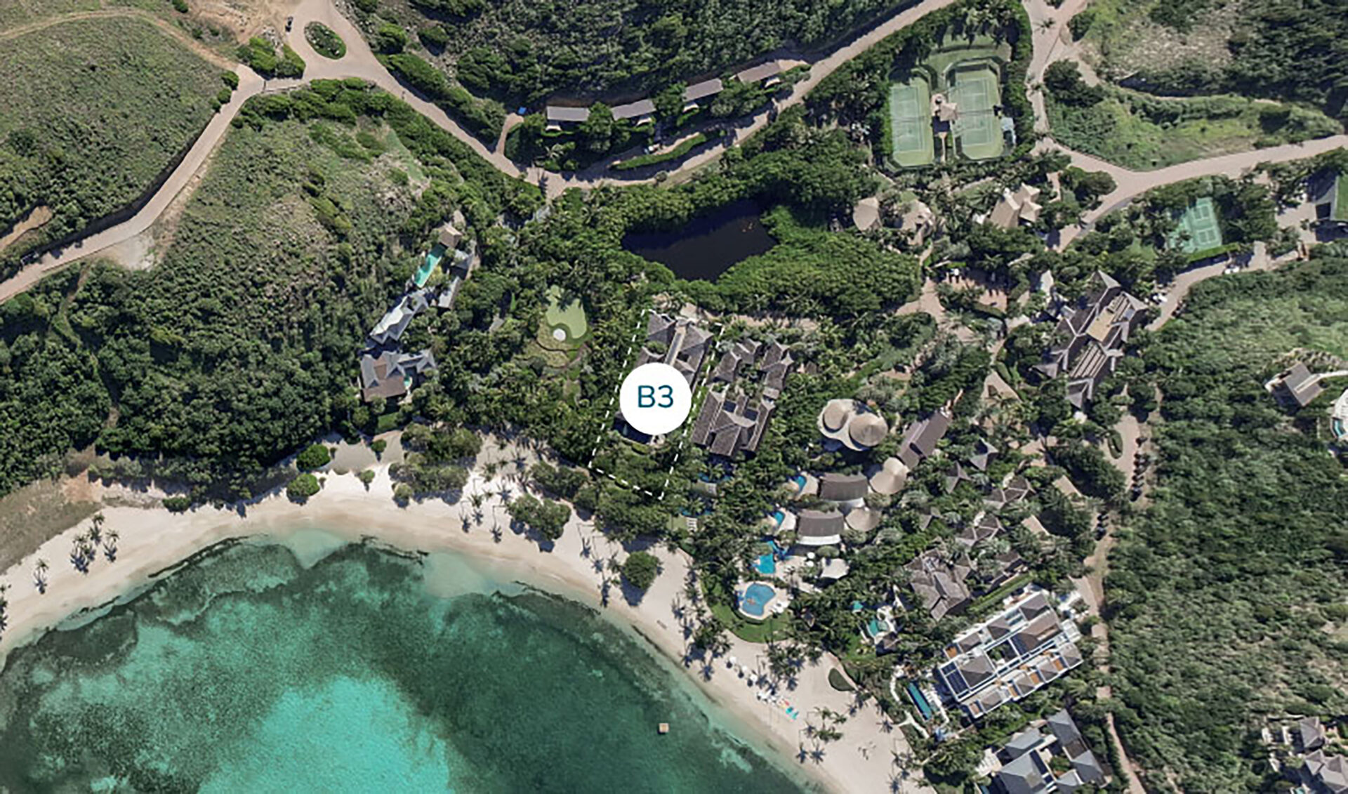 Aerial view of Bella Beach Villa, a tropical resort with a sandy beach and turquoise waters. The landscape includes lush greenery, various buildings, and recreational areas like tennis courts and a swimming pool. A label "B3" is prominent in the center of the image.