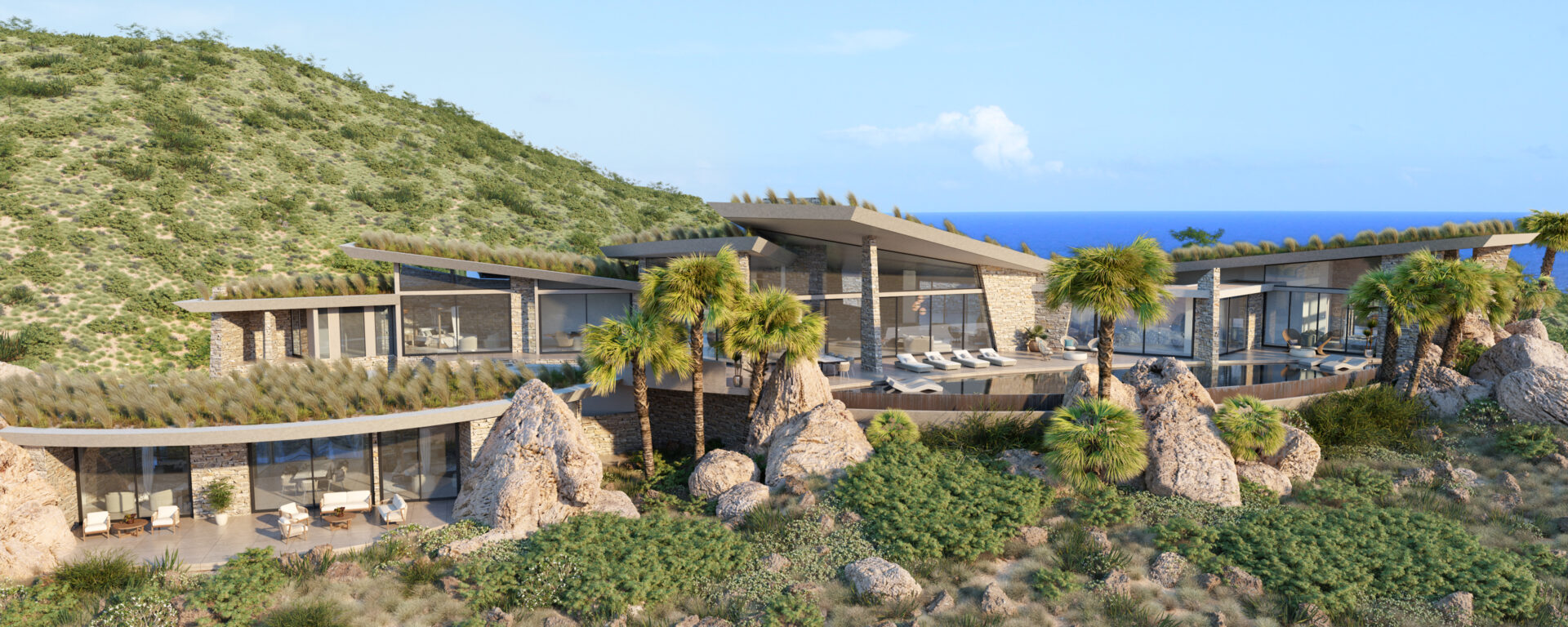 A modern hillside villa, set on a Boulder Homesite, boasts expansive glass windows and a minimalist design. Nestled among rocky terrain and lush greenery, the ocean is visible in the background under a clear blue sky with palm trees framing the property.